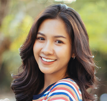 woman wearing a striped shirt with voluminous long brown curly hair smiling in front of a nature-themed background