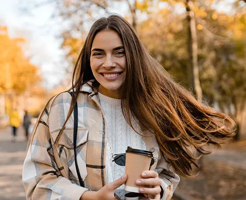 Young smiling woman walking in autumn park with coffee wearing checkered coat, happy mood, fashion style trend, long brown hair