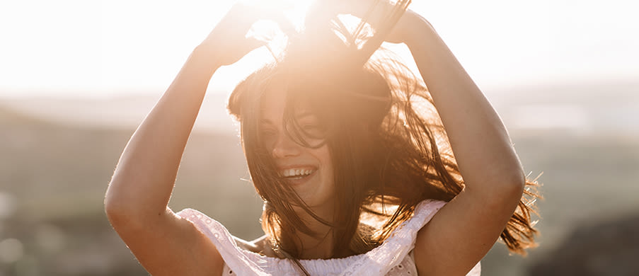 Beautiful girl remains on top of a mountain and looks at the horizon with a beautiful background. A colorful photo of a natural sunset, a miracle, incredible, a dance, hair in the wind.