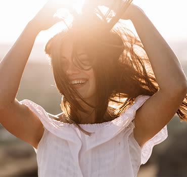 Beautiful girl remains on top of a mountain and looks at the horizon with a beautiful background. A colorful photo of a natural sunset, a miracle, incredible, a dance, hair in the wind.
