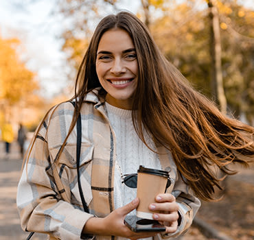Young smiling woman walking in autumn park with coffee wearing checkered coat, happy mood, fashion style trend, long brown hair