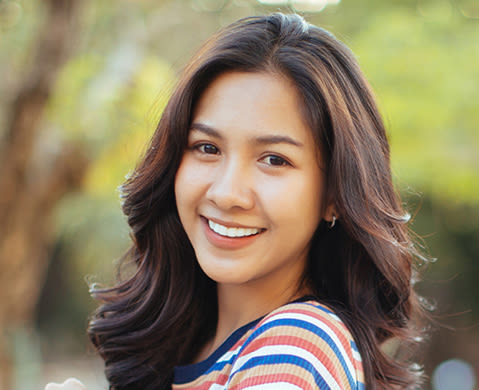 woman wearing a striped shirt with voluminous long brown curly hair smiling in front of a nature-themed background