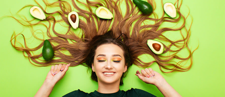 Happy funny girl lying on colored background with avocado fruits on long hair, young woman smiling, female cheerful