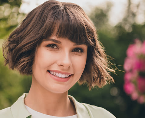Woman with bangs and short brown hair smiling in front of a nature themed flower background