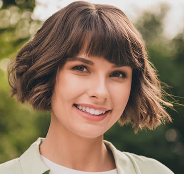 Woman with bangs and short brown hair smiling in front of a nature themed flower background