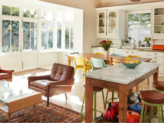 Kitchen and living room, large windows with sun shining in, tables and chairs