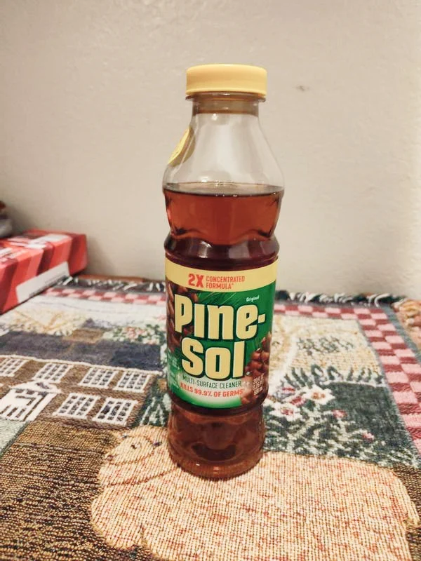 Botella parcialmente usada de Pine-Sol Original Pine sobre una superficie con múltiples dibujos.