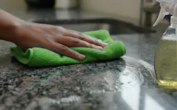 A hand wiping a granite countertop with a blue towel
