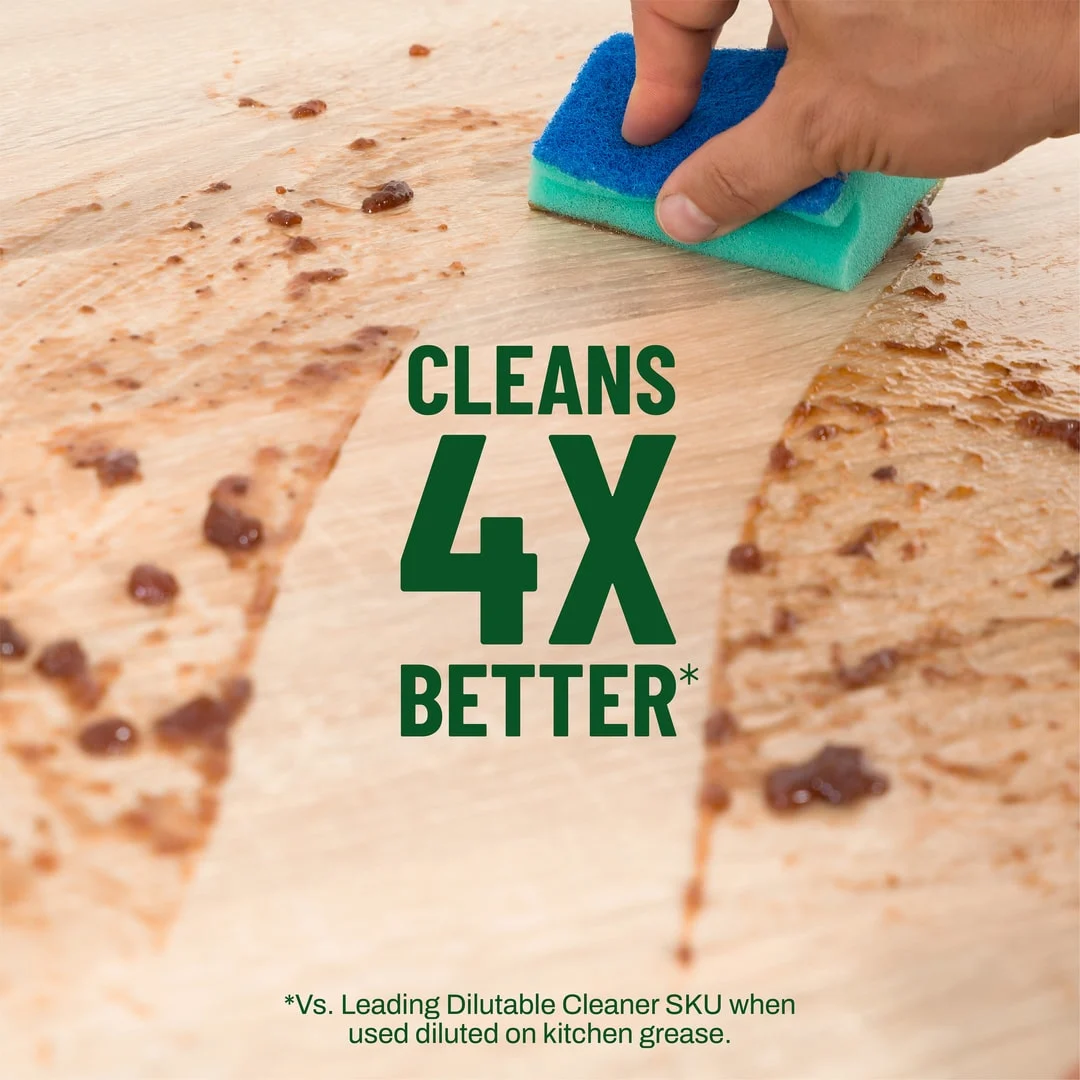Hand wiping a spill of a wooden surface. The words "Cleans 4X Better" appear in the clean part of the spill.
