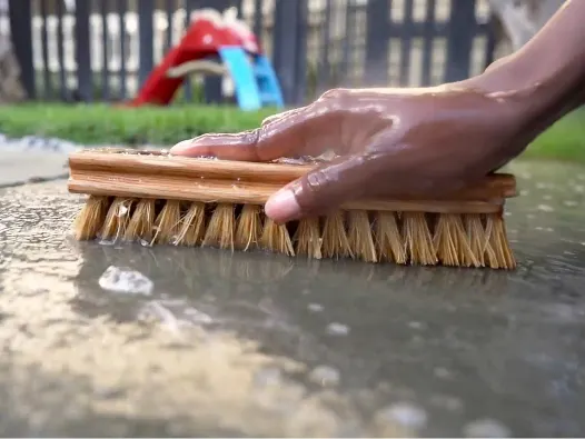 A person scrubbing concrete outdoors with a scrub brush