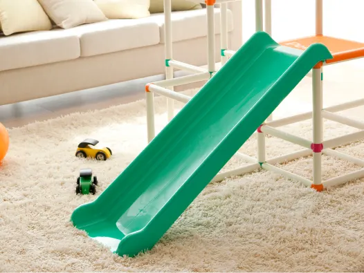 Pequeño tobogán de plástico verde en una sala de estar alfombrada