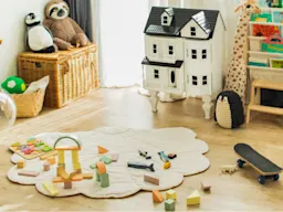 Una sala de juegos infantil con casa de muñecas, peluches, bloques y patineta.