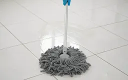 A gray circular mop being used on white tile floor