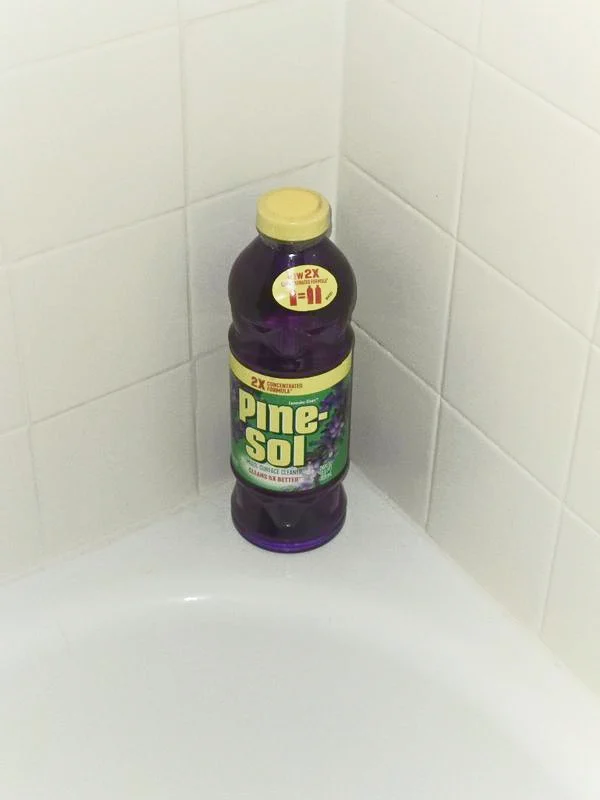 Botella de limpiador Lavender Clean Pine-Sol en la esquina de la bañera con azulejos blancos.