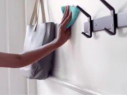 Hand wiping a wall with coat hooks and hanging purse with a turqoise cloth