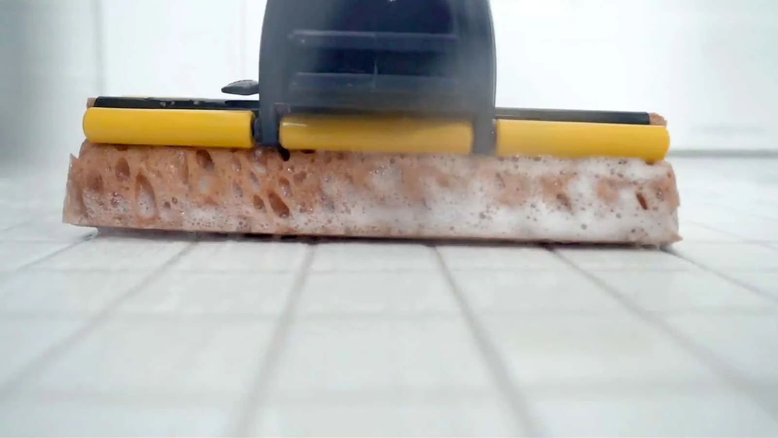 Close-up of soapy sponge mop on white tile floor
