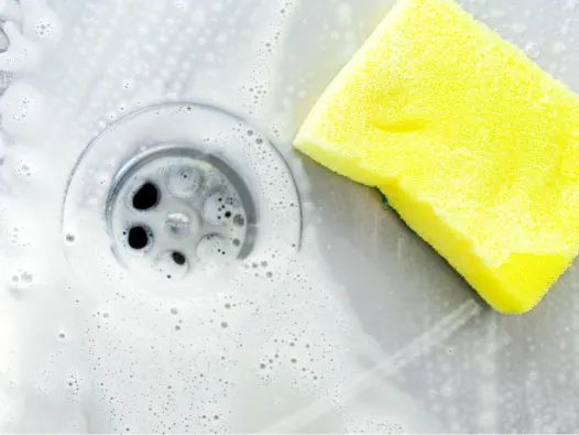 Soapy stainless steel sink and drain with yellow sponge.