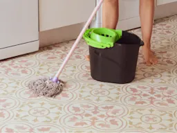 Mopping a patterned linoleum floor with nearby bucket, strainer and bare feet.