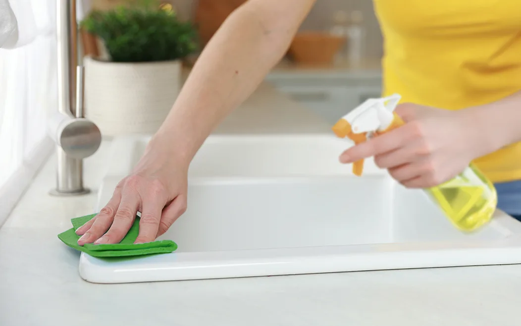 A hand using a green cloth to clean the edge of a kitchen sink