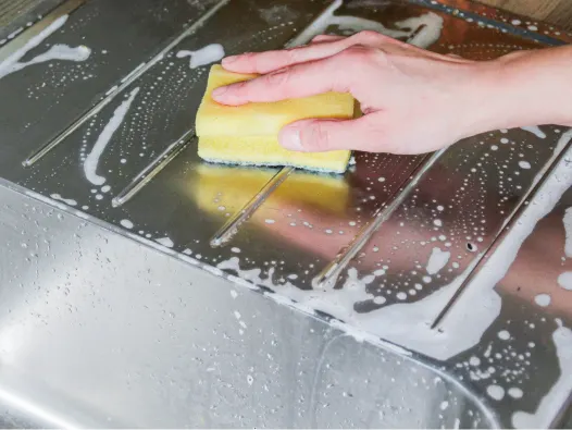 Hand cleaning a sudsy stainless steel surface with a yellow sponge