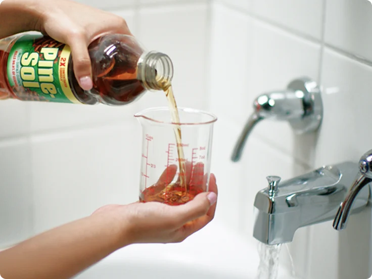 Vertiendo limpiador Pine-Sol Original con aroma a pino en una taza medidora dentro de una bañera.