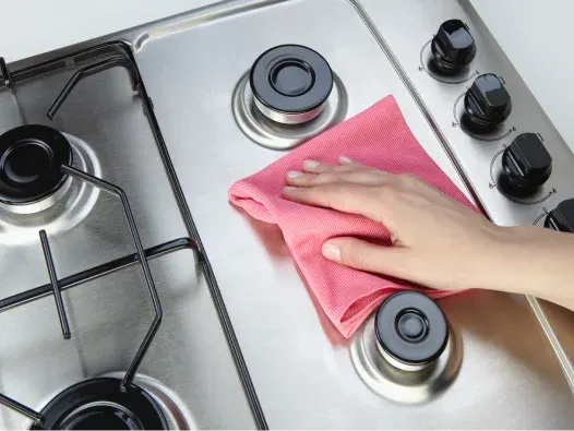 Mano limpiando la estufa con un paño rosa