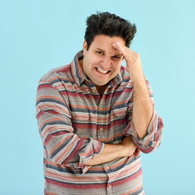 Man in striped button up shirt making a funny expression of stress while standind against a light blue background.