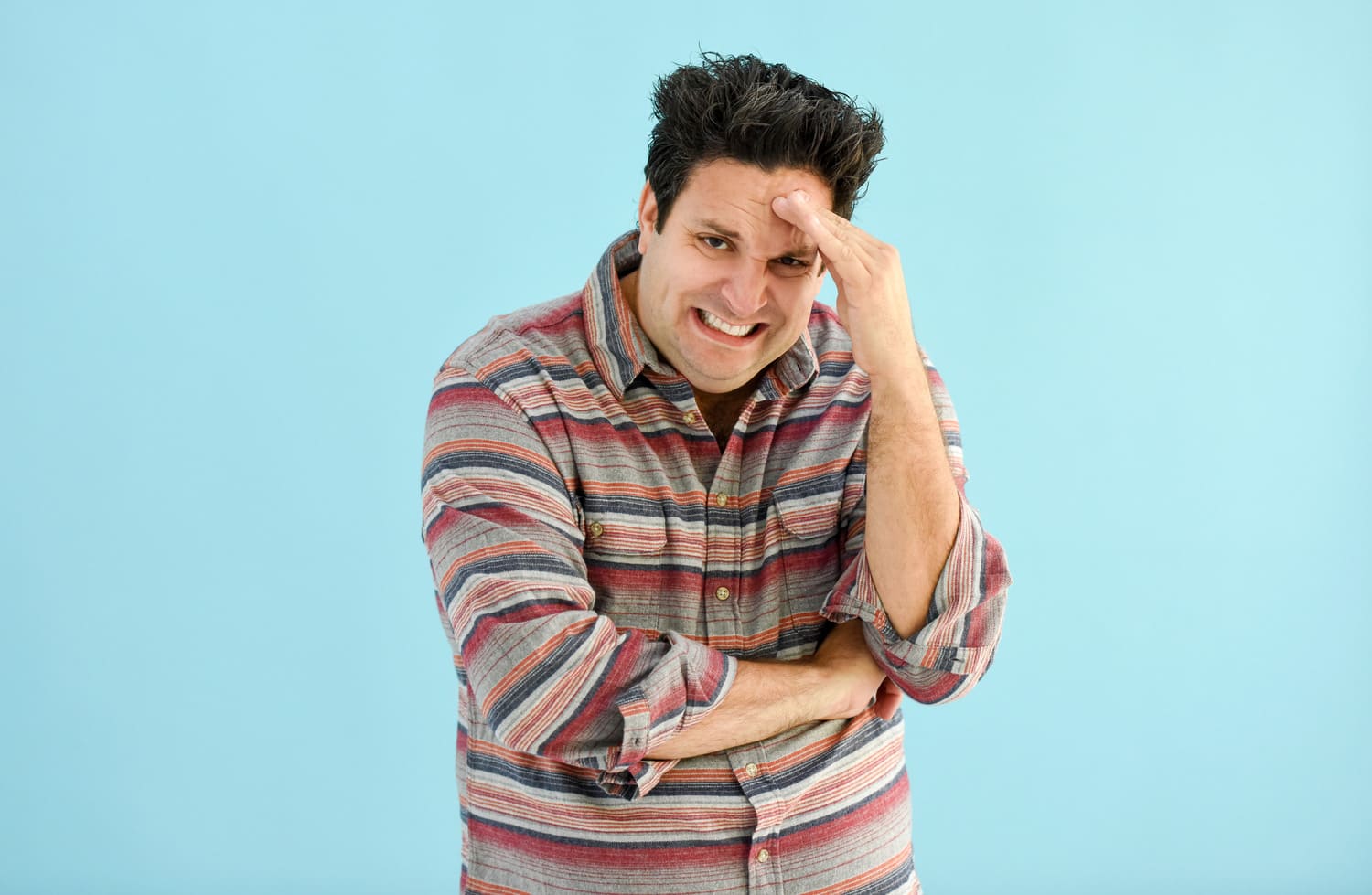 Man pretending to look stressed with hand on forehand and grimacing. 