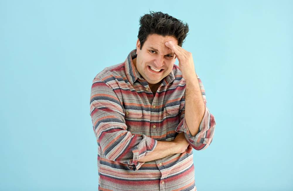 Man pretending to look stressed with hand on forehand and grimacing.