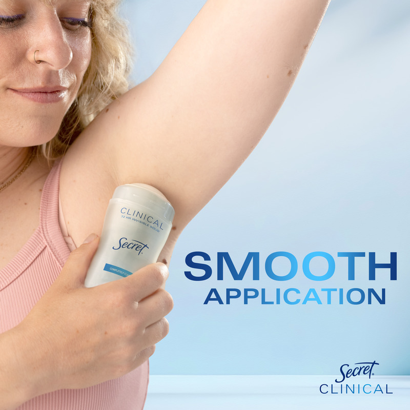 A woman applying Secret Clinical deodorant to her underarm, demonstrating smooth application on a light blue background