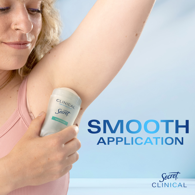 A woman applying Secret Clinical deodorant to her underarm, demonstrating smooth application on a light blue background