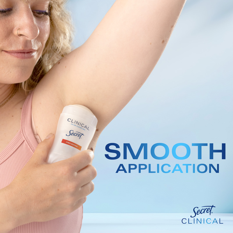 A woman applying Secret Clinical deodorant to her underarm, demonstrating smooth application on a light blue background