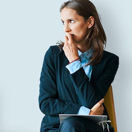 Worried woman sitting with a tablet and touching her face.