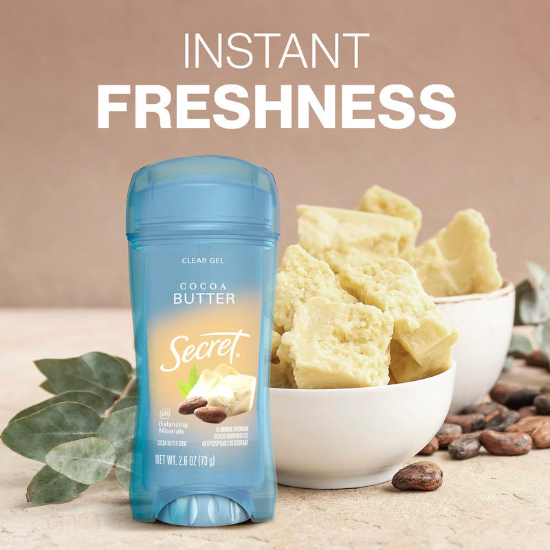 Instant freshness. Secret clear gel deodorant with cocoa butter beside cocoa butter chunks in a bowl and some leaves on a tabletop
