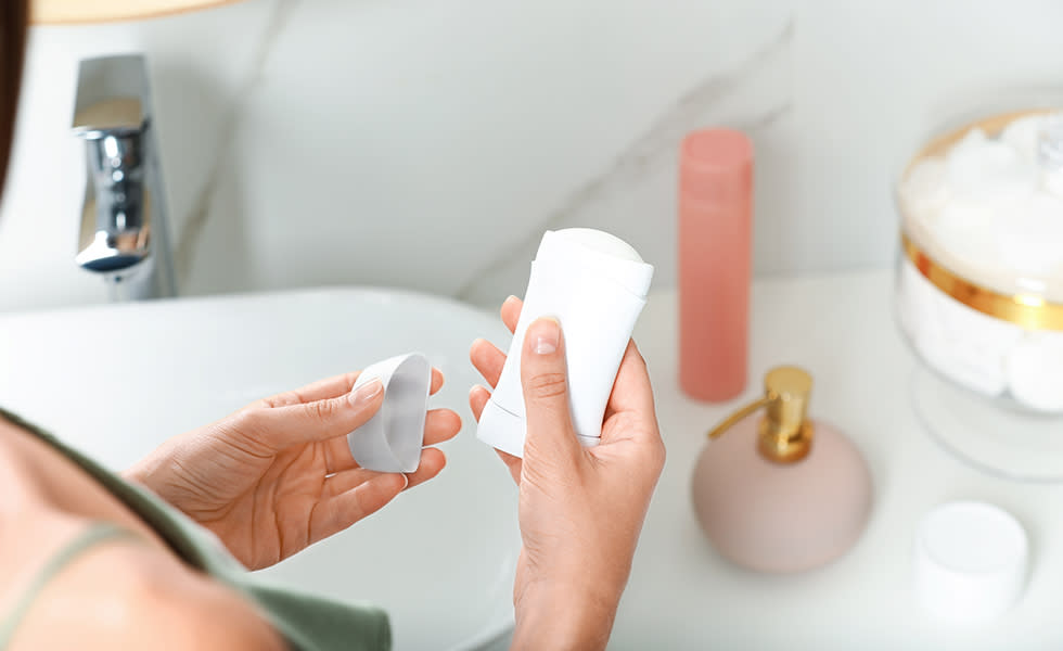 Person holding an open deodorant stick over a bathroom sink.