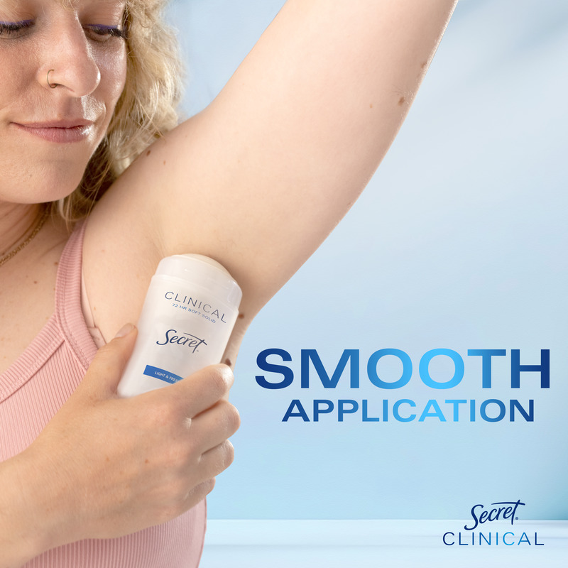 A woman applying Secret Clinical deodorant to her underarm, demonstrating smooth application on a light blue background