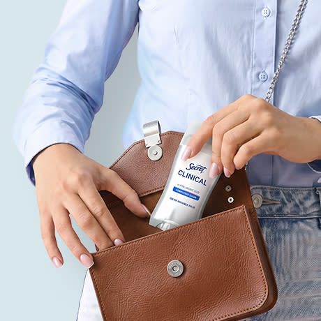 Woman placing a deodorant stick into a brown handbag.
