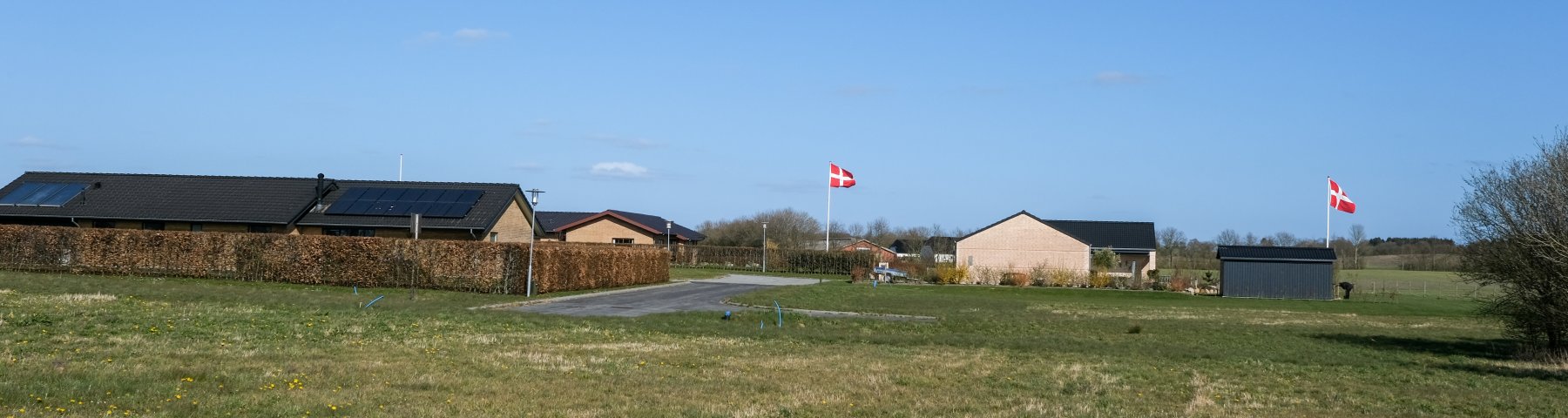 Udstykning med byggegrunde ved Kærvænget i Jordrup. Udstykningen er en grøn græsmark. I baggrunden ses nabovænget med huse og 2 flagstænger med Dannebrog oppe