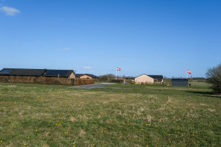 Udstykning med byggegrunde ved Kærvænget i Jordrup. Udstykningen er en grøn græsmark. I baggrunden ses nabovænget med huse og 2 flagstænger med Dannebrog oppe