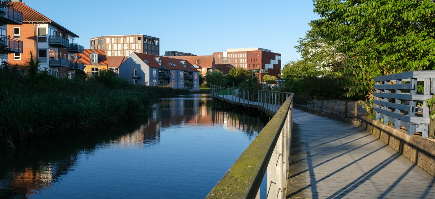 Kolding Å, der løber gennem midtbyen i Kolding, med en gangbro i højre side af billedet og byens huse til venstre på den anden side af åen