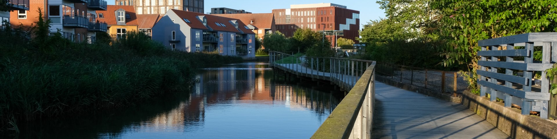 Kolding Å, der løber gennem midtbyen i Kolding, med en gangbro i højre side af billedet og byens huse til venstre på den anden side af åen