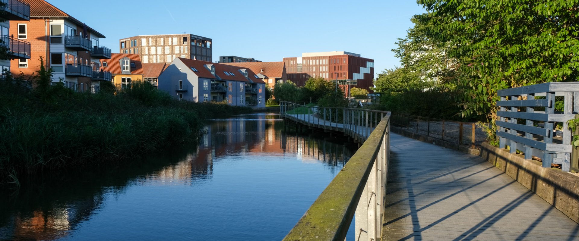 Kolding Å, der løber gennem midtbyen i Kolding, med en gangbro i højre side af billedet og byens huse til venstre på den anden side af åen