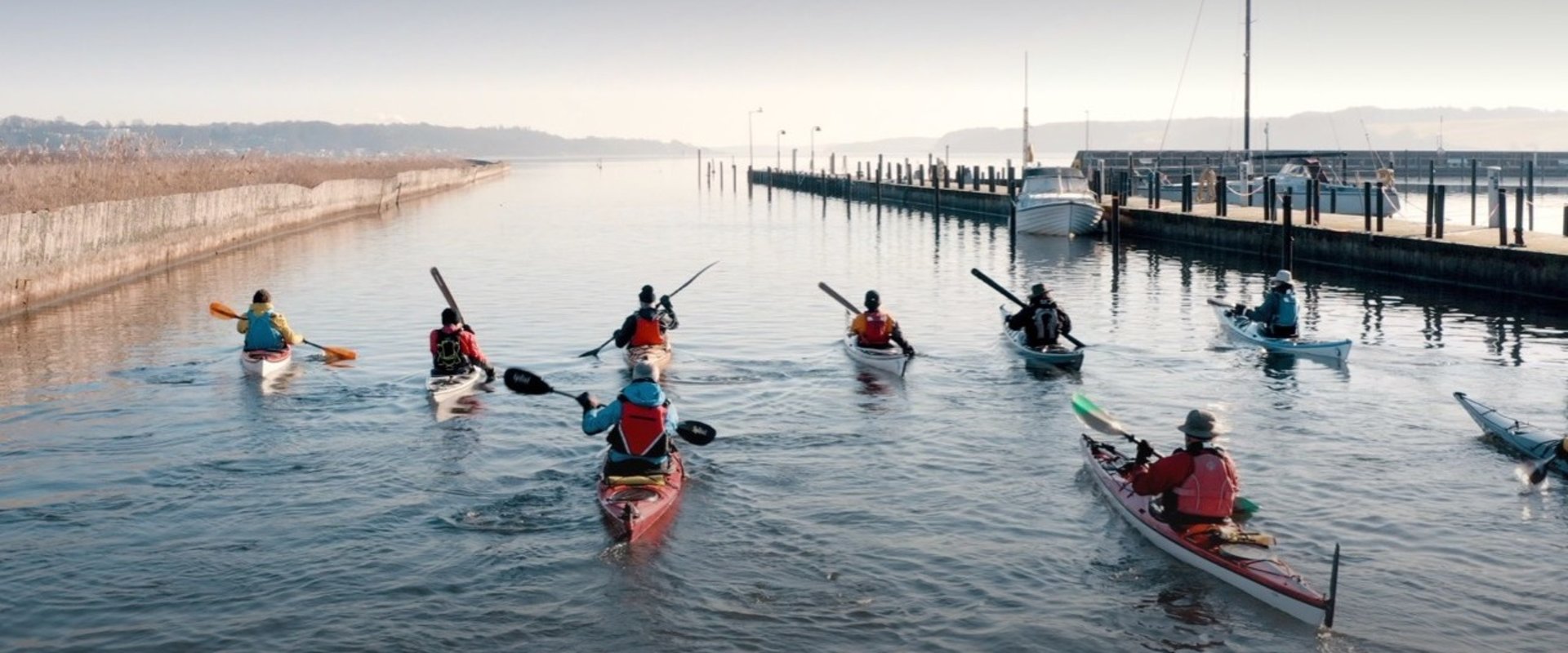 Ni kajakker på vandet på vej ud mod Kolding Fjord fra kajakklubben ved Kolding Å og Havn med lystbådehavnen til højre i billedet