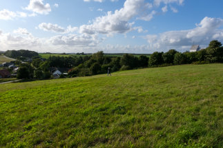 Landskabelig udsigt over et stykke landbrugsjord til salg ved Harte vest for Kolding med blå himmel og drivende, hvide skyer