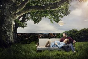 Et par sidder og ligger i en sofa, der står i det grønne under et træ med udsigt til Kolding by i baggrunden