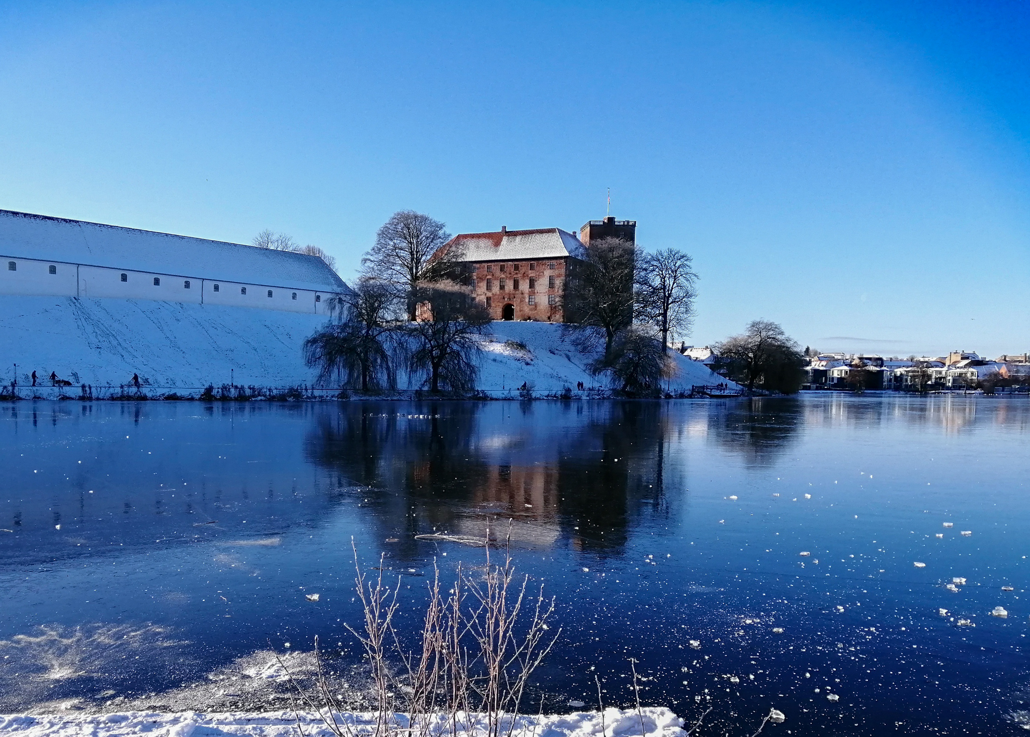 Vinterlandskab med Koldinghus og Staldgaarden i baggrunden og Slotssøens tilfrosne isblå overflade i forgrunden