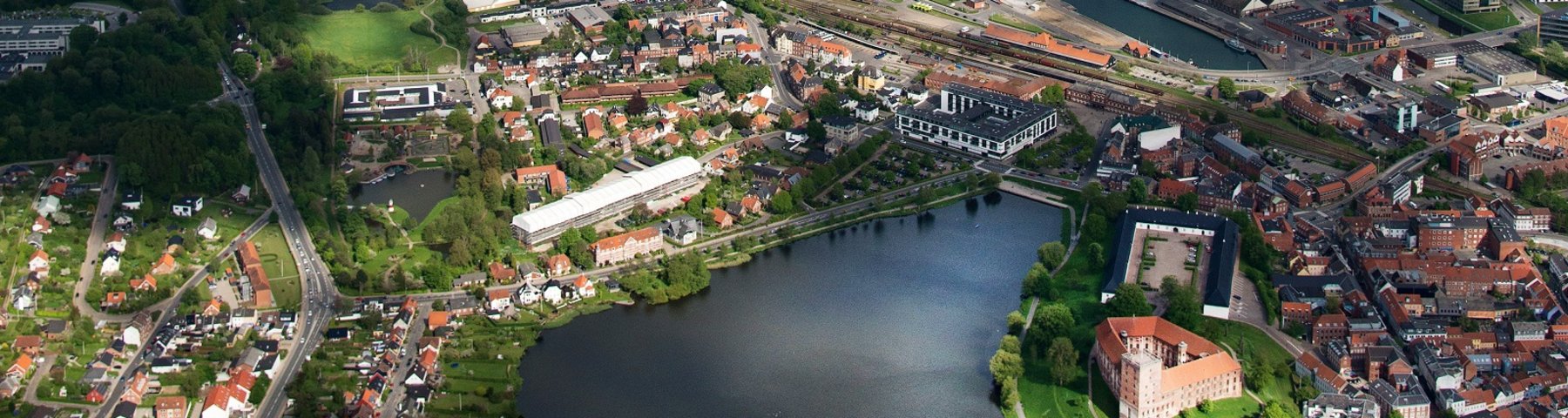 Kolding set fra oven med Koldinghus og Slotssøen lidt under midt i billedet og fjord og haven øverst i billedet. 