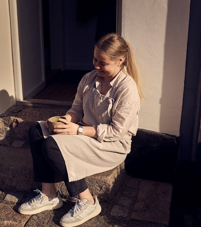 Maria Grønborg sidder på trappestenen til sit sæbeværksted og holder pause med en kop mellem hænderne