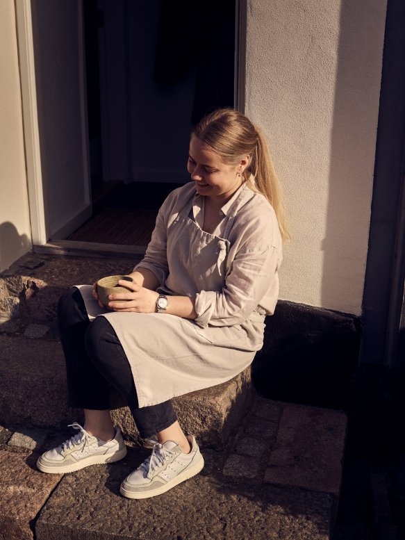 Maria Grønborg sidder på trappestenen til sit sæbeværksted og holder pause med en kop mellem hænderne