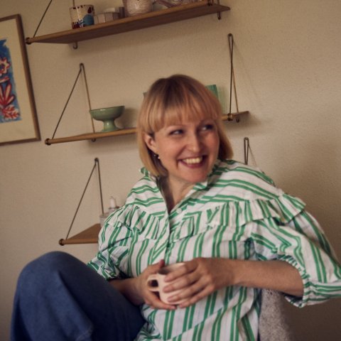 Pia Elgaard sidder på en stol i sin lejlighed og smiler med en kaffekop mellem hænderne